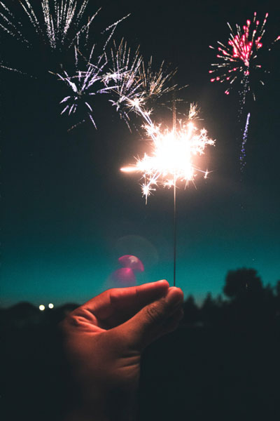 a lit sparkler with a background of fireworks